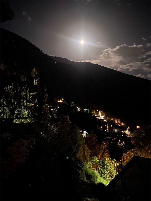 A bright moon over dark hills at night, with the lights of a small town below